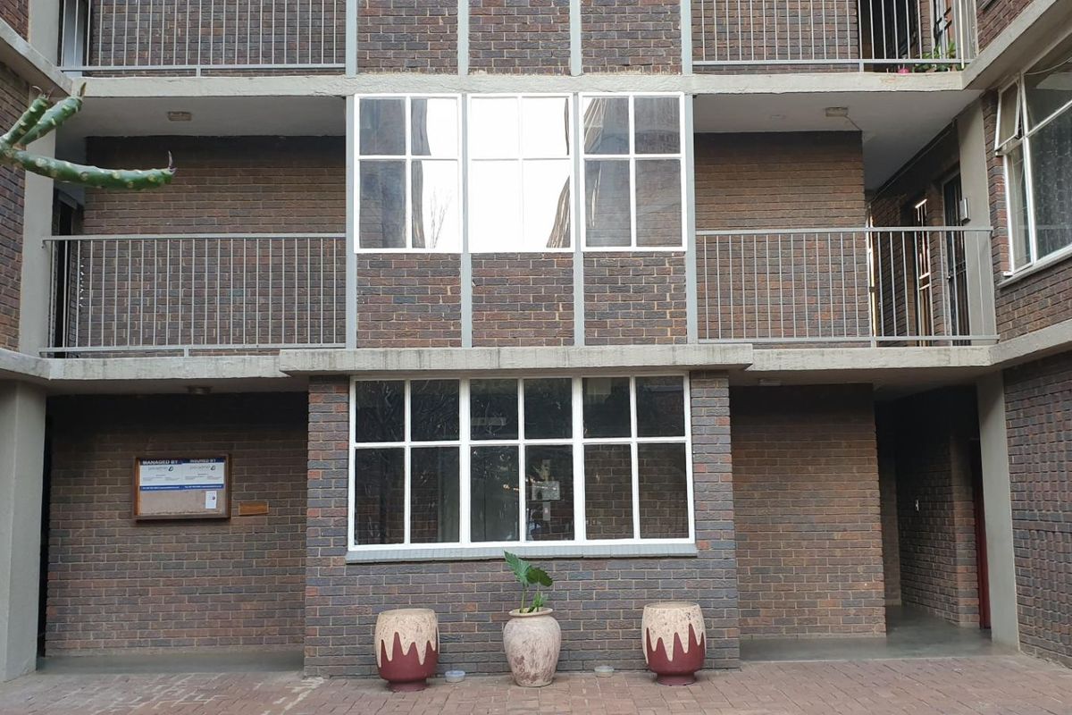 Exterior view of a multi-story apartment building featuring face-brick facade, metal balcony railings, and large multi-pane windows.