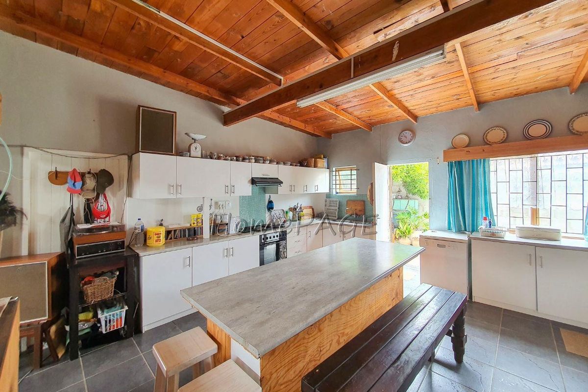 Rustic kitchen featuring exposed timber beam ceiling, central island with stone-look countertop, white cabinetry, and direct access to the rear garden area.