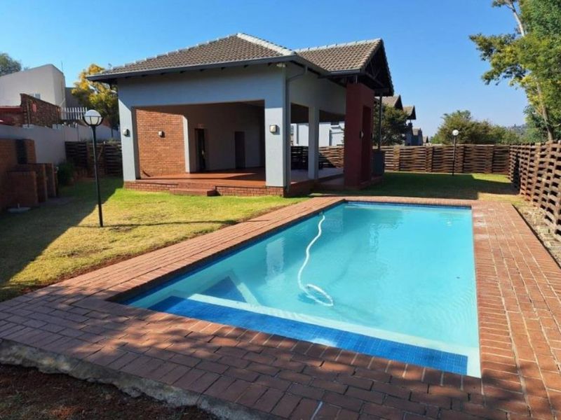 A well-maintained outdoor area featuring a swimming pool with brick coping, adjacent to a covered patio and landscaped garden space.