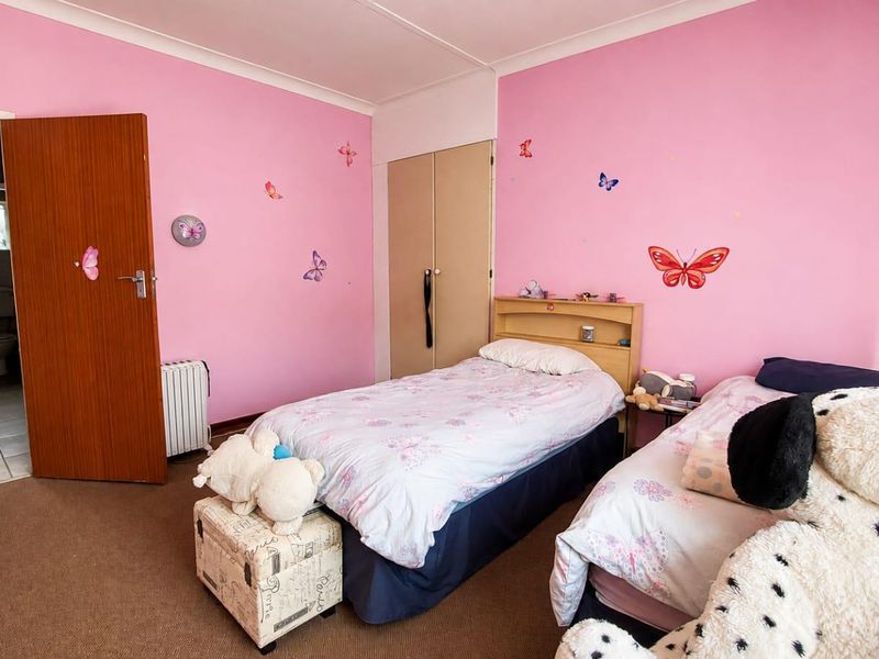 A bedroom featuring pink walls, carpeted flooring, and a built-in cupboard, with an adjacent view into a bathroom.