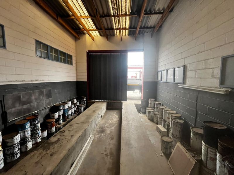 Industrial utility space featuring a central concrete inspection pit, high ceilings with translucent roof panels, and durable painted brick walls.