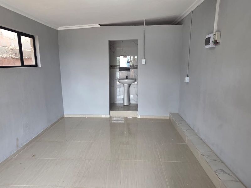 An empty bedroom featuring tiled flooring, a small integrated basin area, and basic finishes, offering a blank canvas for potential renovation or styling.