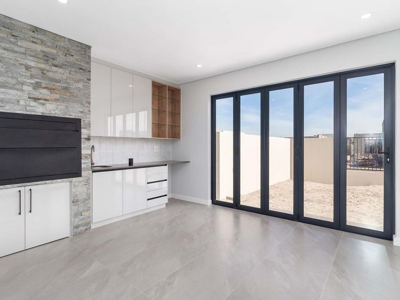 Modern open-plan living area featuring a built-in braai with stone cladding, sleek gloss cabinetry, and large stacking doors opening to the rear yard.