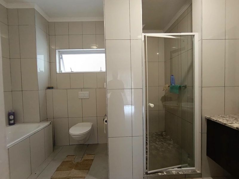 Modern bathroom featuring a wall-mounted toilet, built-in bathtub, and a separate glass-enclosed shower with neutral tiled finishes throughout.