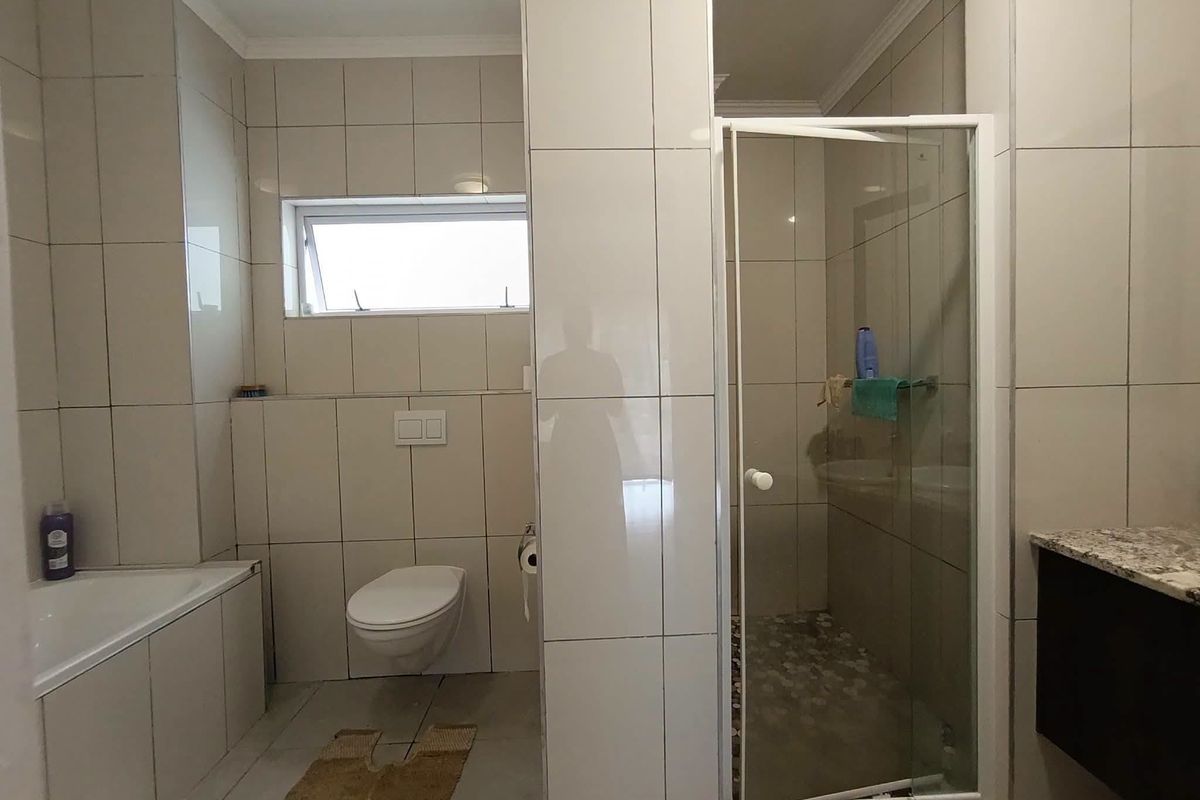 Modern bathroom featuring a wall-mounted toilet, built-in bathtub, and a separate glass-enclosed shower with neutral tiled finishes throughout.
