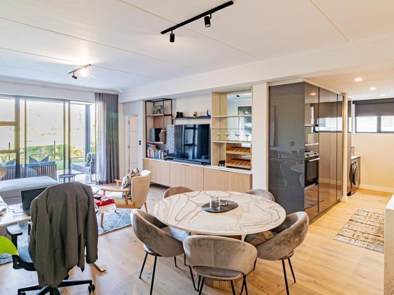 Modern open-plan living area featuring a sleek kitchen with stone island, integrated appliances, and seamless flow to the outdoor patio through sliding glass doors.