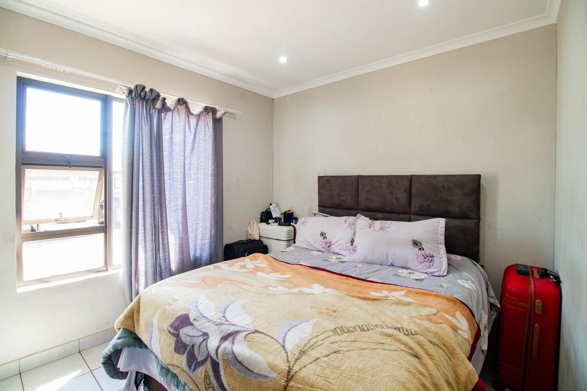 A functional bedroom featuring tiled flooring, recessed downlighting, and an aluminium window frame, providing a neutral base for potential interior updates.