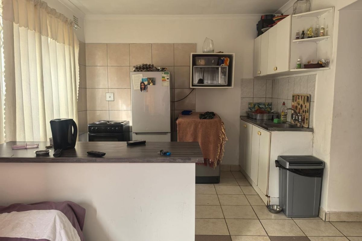 A compact kitchen featuring tiled flooring, built-in cabinetry, a breakfast bar, and a tiled splashback, offering a functional layout with potential for modernization.