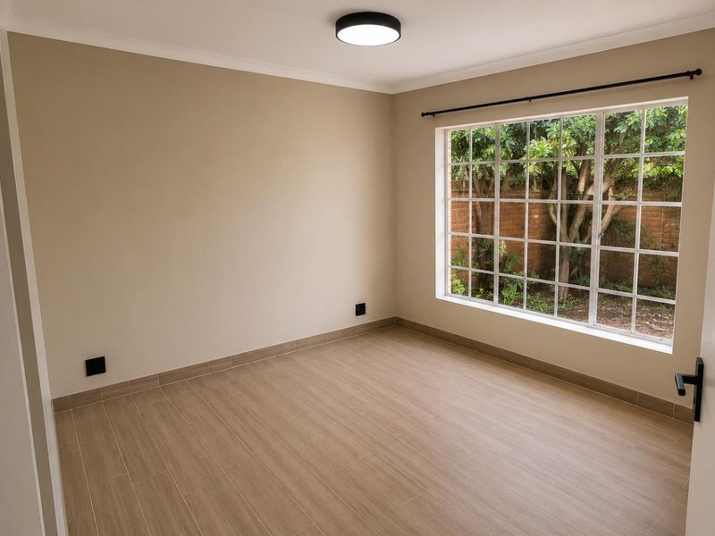 A bright, empty bedroom featuring modern tiled flooring, a large grid-pattern window overlooking the garden, and neutral wall finishes.