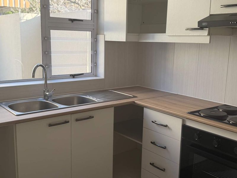 A clean, functional kitchen featuring modern white cabinetry, laminate countertops, a double bowl sink, and integrated cooking appliances.