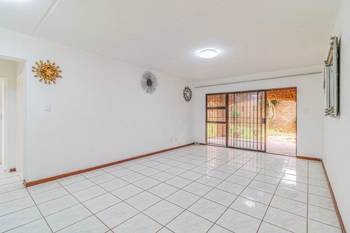 A bright, empty living room featuring white tiled flooring and a sliding glass door with a security gate leading to the rear garden.