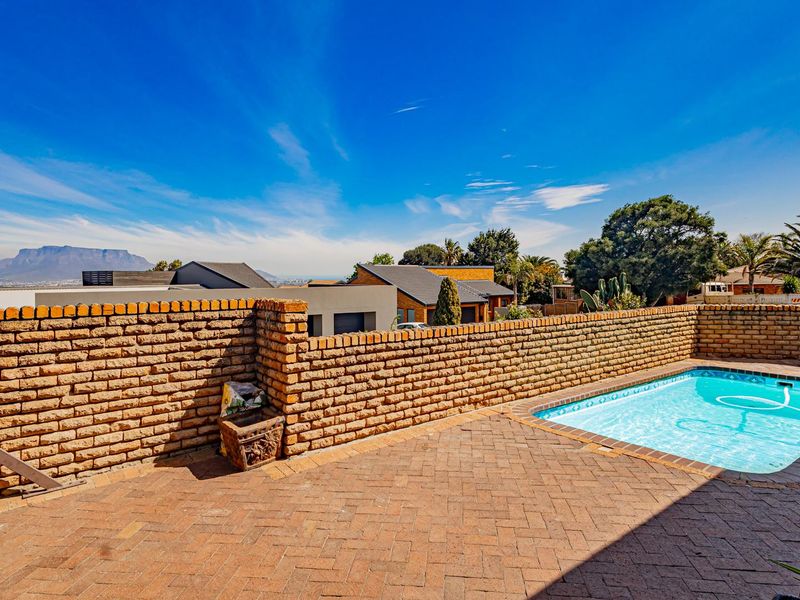 Outdoor pool area featuring a brick-paved patio, a swimming pool, and a brick boundary wall with scenic mountain views in the background.