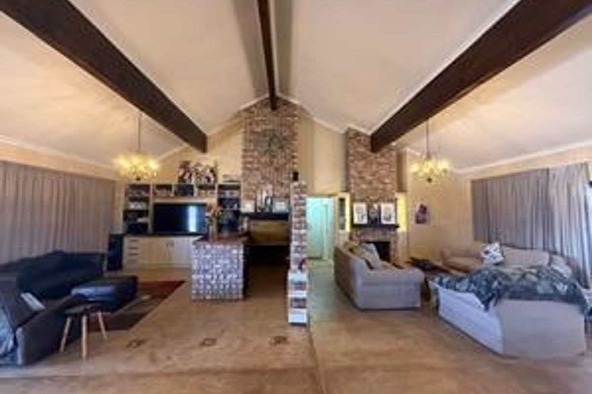 Spacious living area featuring vaulted ceilings with exposed timber beams, dual brick fireplaces, and built-in cabinetry, offering a classic architectural aesthetic.