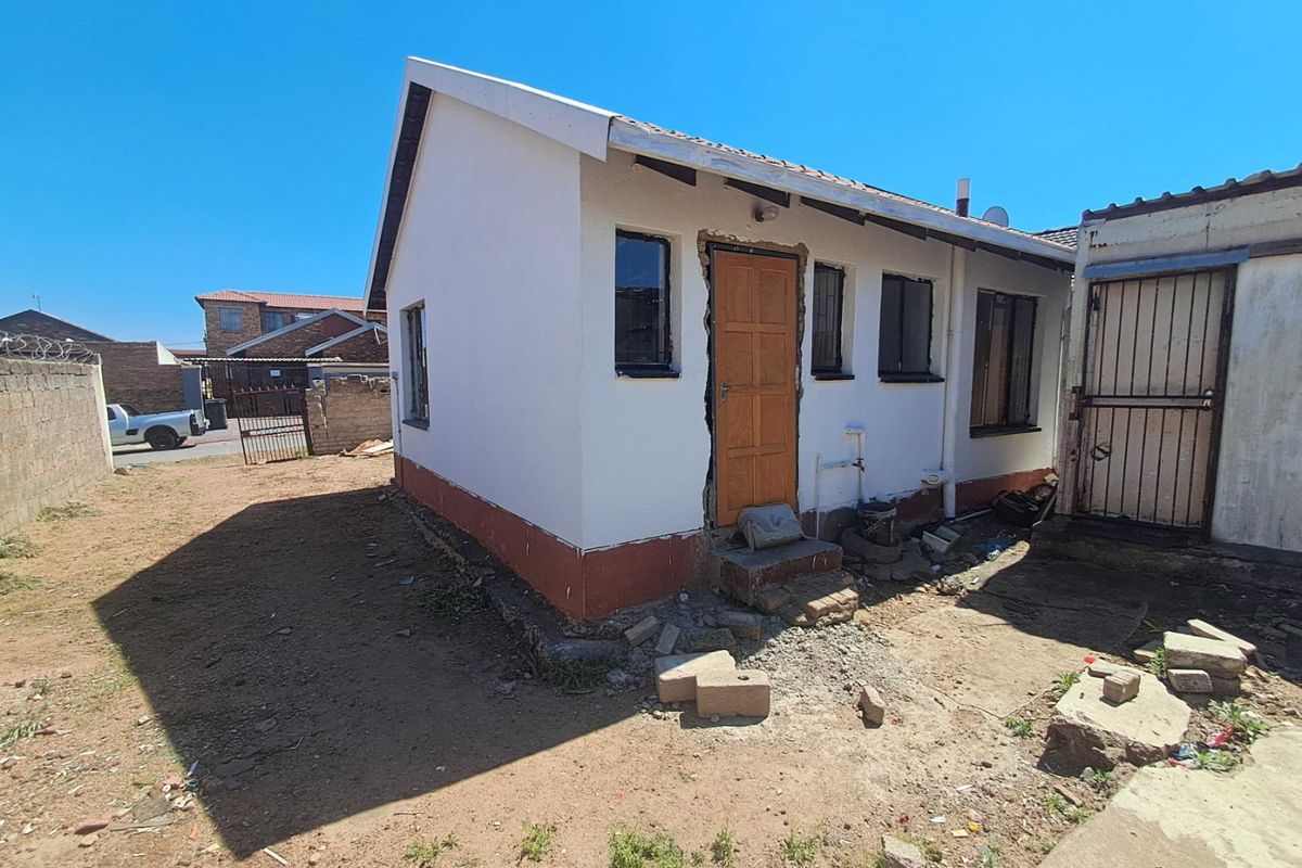 Rear view of a detached residential structure showing unfinished exterior wall finishes, exposed door frame masonry, and surrounding unlandscaped yard area.