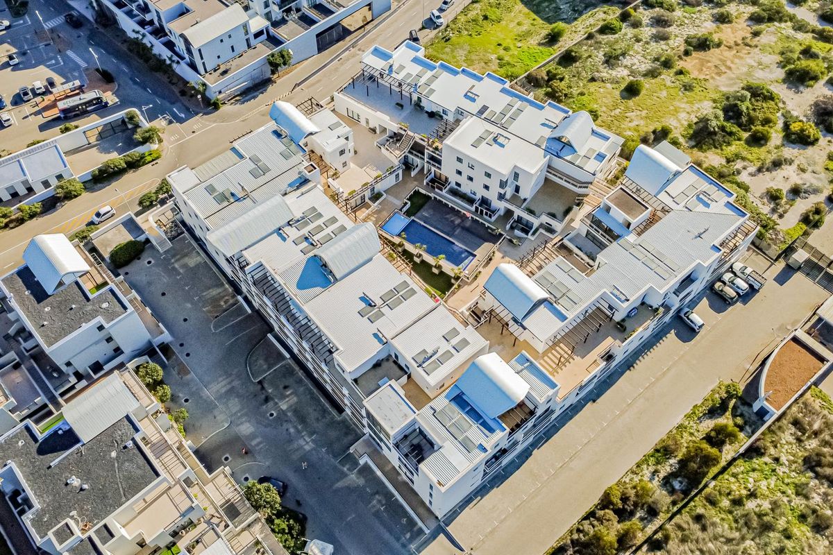 Aerial view of a modern apartment complex featuring a central swimming pool, paved courtyard, and solar-equipped metal roofing.