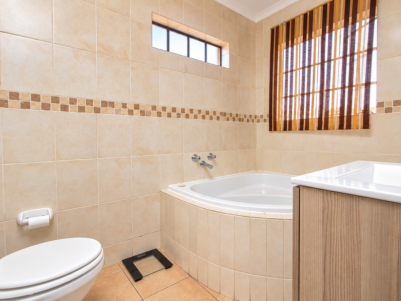 A well-maintained bathroom featuring a built-in corner bathtub, vanity cabinet, and neutral ceramic tiling throughout.
