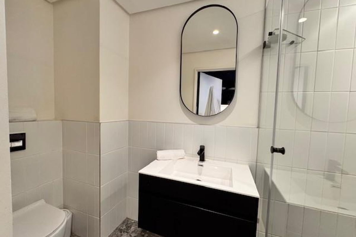 Modern bathroom featuring a wall-mounted vanity with a basin, a frameless glass shower enclosure, and a wall-hung toilet with contemporary black fixtures.