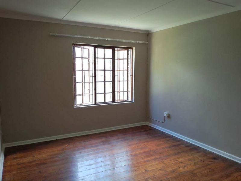 An empty bedroom featuring polished wooden flooring, neutral wall tones, and a window fitted with security burglar bars.