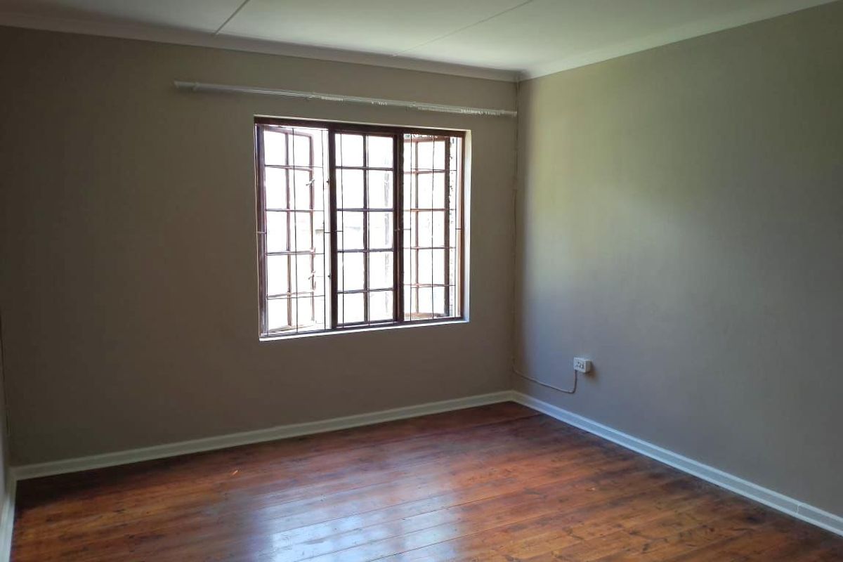 An empty bedroom featuring polished wooden flooring, neutral wall tones, and a window fitted with security burglar bars.