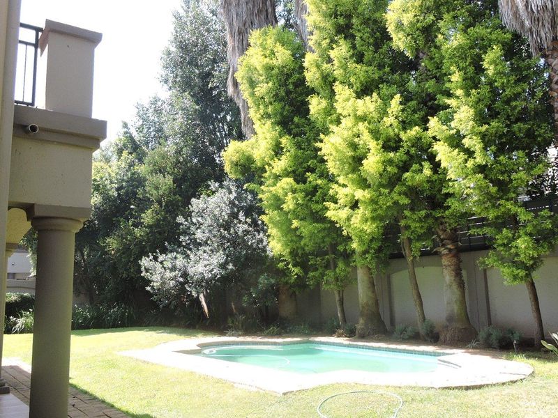 A private backyard featuring a swimming pool, paved surround, and established trees, overlooked by a covered patio area.