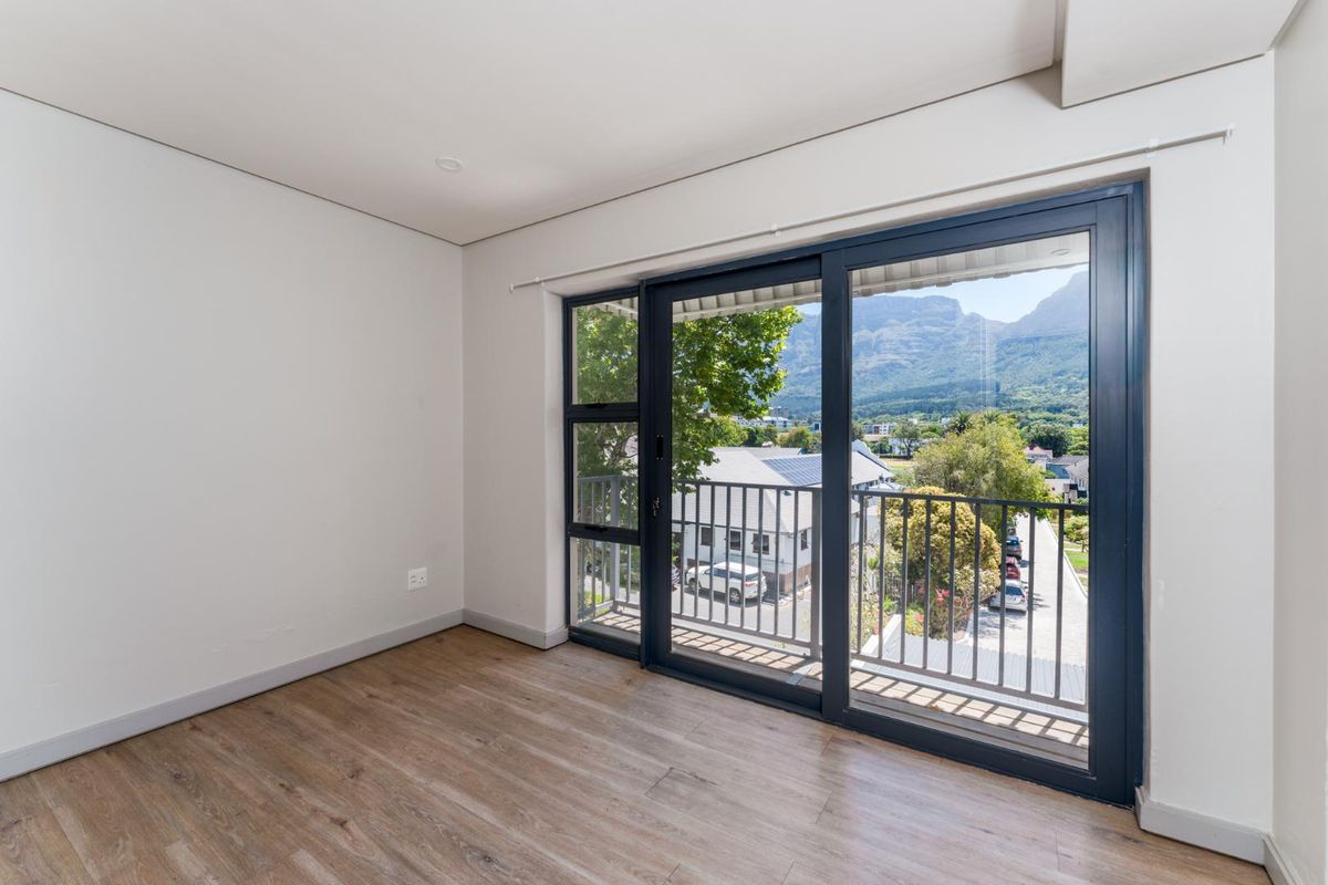An empty bedroom featuring modern laminate flooring and a large sliding glass door that opens onto a balcony with scenic mountain views.