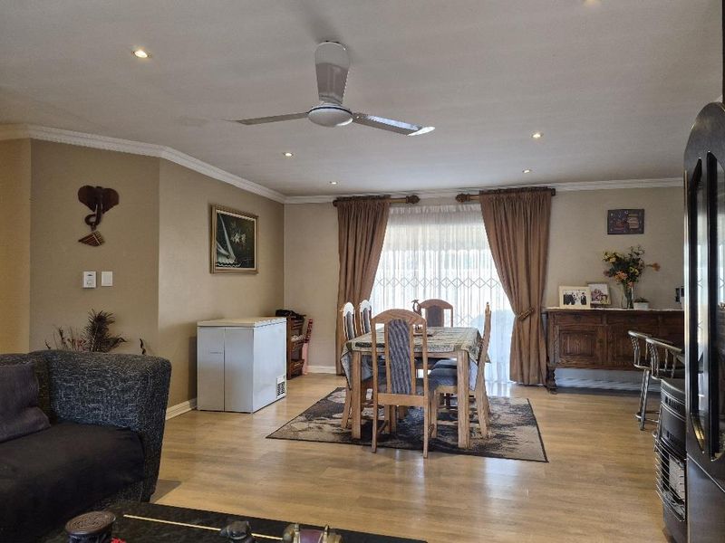Spacious open-plan living and dining area featuring laminate flooring, recessed downlights, a ceiling fan, and a security gate leading to the exterior.