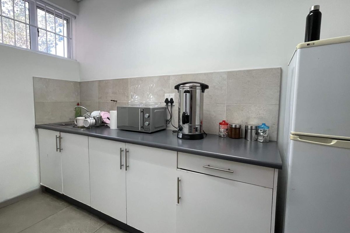 A functional office kitchenette featuring white cabinetry, a grey laminate countertop, tiled backsplash, and a stainless steel sink.