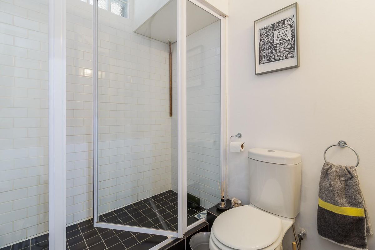 A clean bathroom featuring a glass-enclosed shower with white subway tiles, dark floor tiles, and a standard toilet.