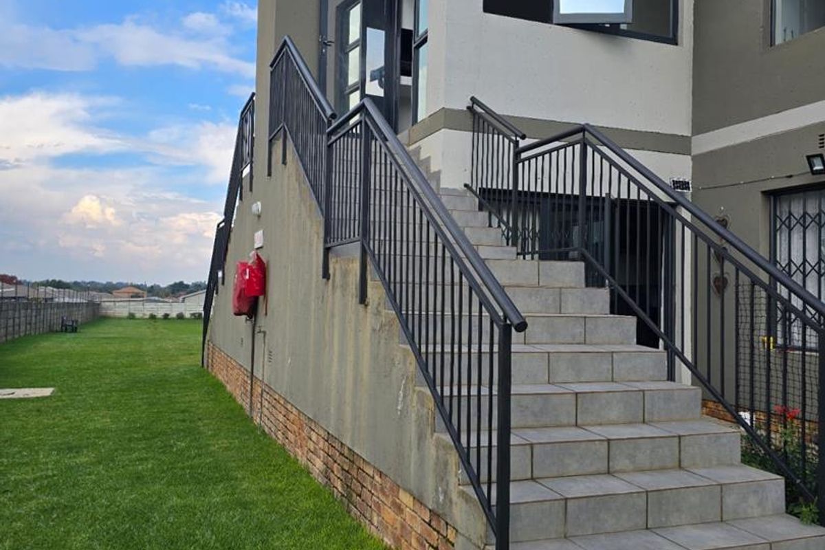 Exterior view of an apartment building featuring an external tiled staircase with metal railings leading to an upper-level entrance, adjacent to a lawn area.