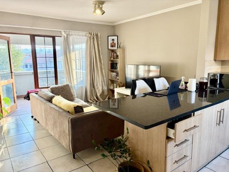 Open-plan living area featuring a kitchen with granite countertops and tiled flooring, leading directly to an outdoor balcony through a sliding glass door.