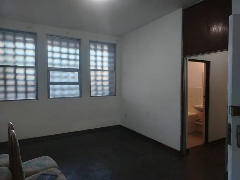 A vacant bedroom featuring timber flooring and glass block windows, with an adjacent en-suite bathroom visible through the doorway.