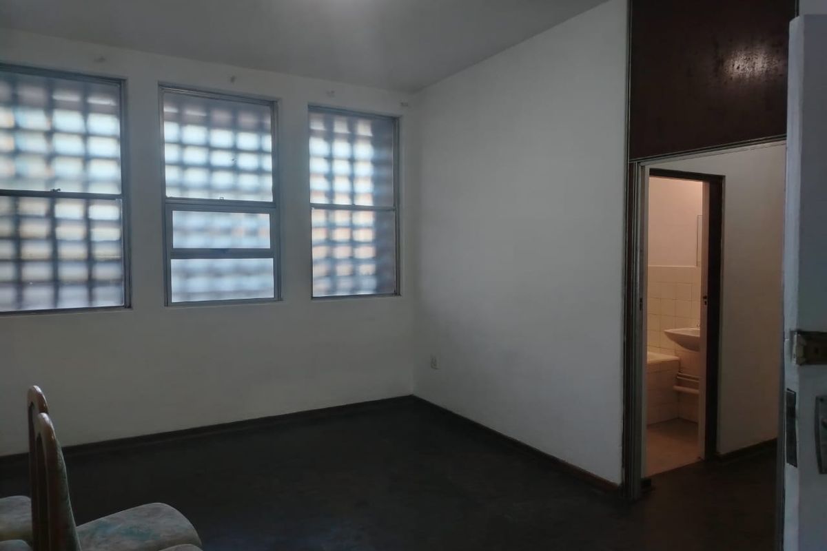 A vacant bedroom featuring timber flooring and glass block windows, with an adjacent en-suite bathroom visible through the doorway.