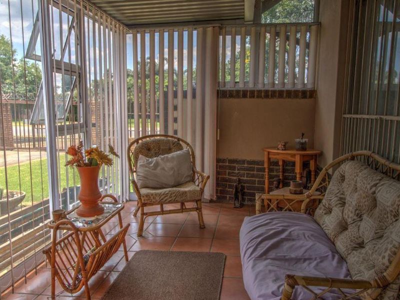 A covered patio area featuring tiled flooring, brick wall accents, and security bars, providing a functional outdoor living space.