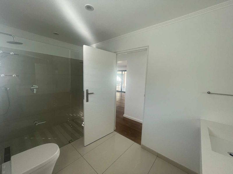 Modern bathroom featuring a walk-in shower with glass screen, wall-hung toilet, and vanity basin, finished with neutral floor tiles and recessed lighting.