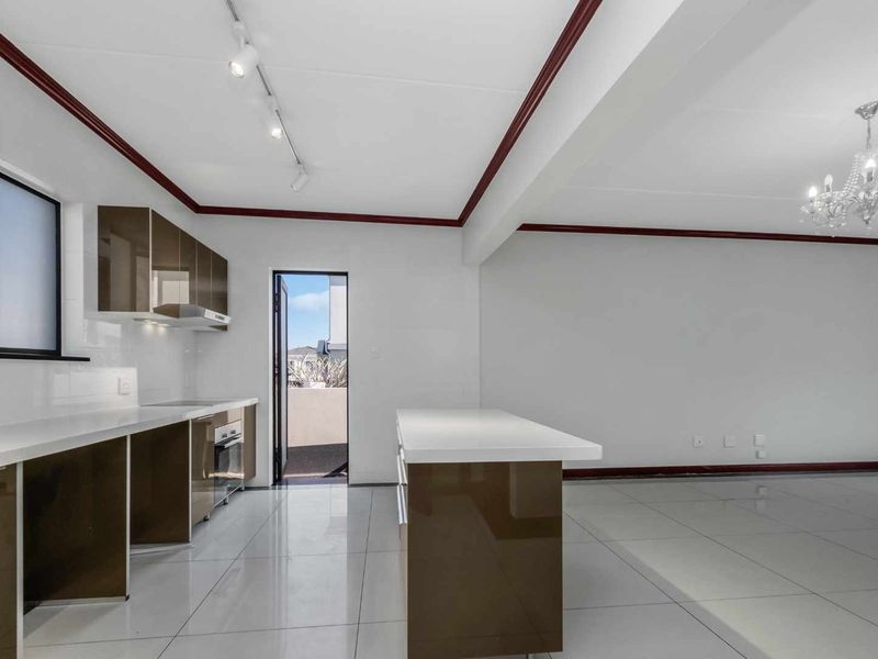 Spacious open-plan kitchen and living area featuring modern glossy cabinetry, stone countertops, a central island, and polished tiled flooring.