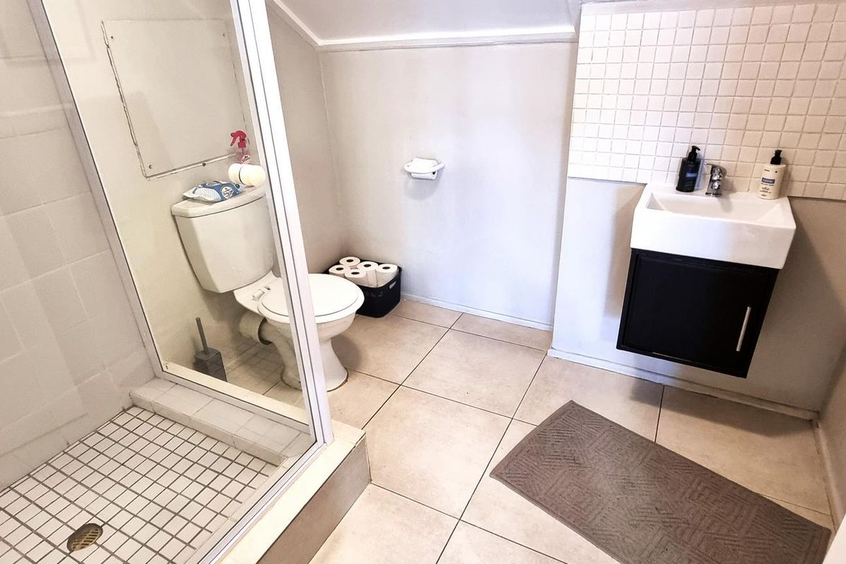 Compact office bathroom featuring a glass-enclosed shower, wall-mounted vanity basin with tiled splashback, and a standard toilet.