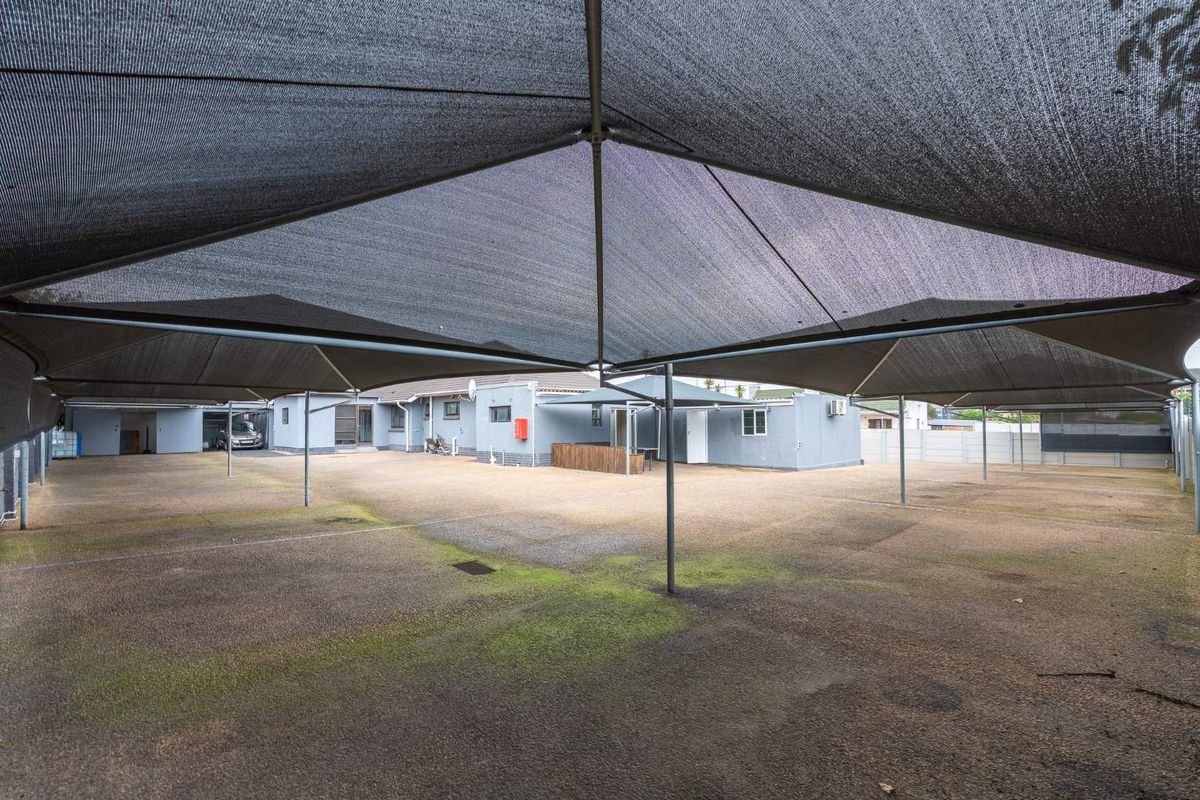 A spacious paved rear courtyard area featuring an extensive overhead shade cloth structure, providing ample covered parking or outdoor utility space.