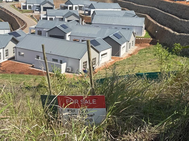 An elevated view of a residential estate development featuring modern homes, paved roads, and tiered retaining walls, with a for sale sign in the foreground.