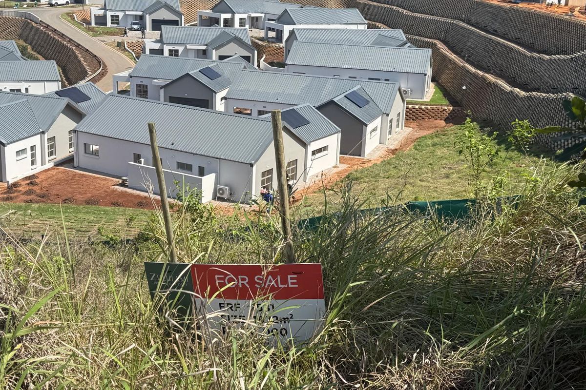 An elevated view of a residential estate development featuring modern homes, paved roads, and tiered retaining walls, with a for sale sign in the foreground.