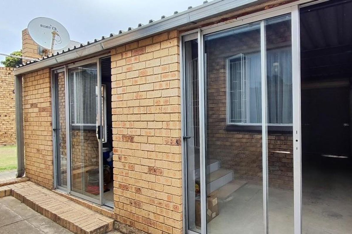 Exterior view of a brick-built structure featuring sliding glass doors, a corrugated roof, and an external satellite dish installation.