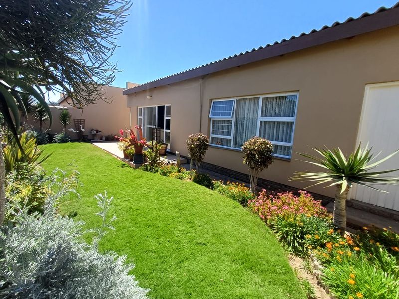 A well-maintained rear exterior view of the house featuring a landscaped garden, paved patio, and aluminium-framed windows.