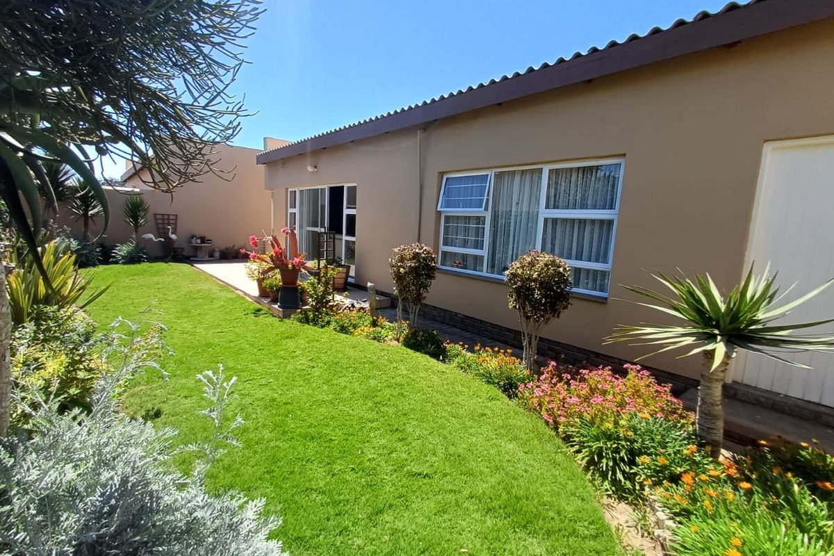 A well-maintained rear exterior view of the house featuring a landscaped garden, paved patio, and aluminium-framed windows.