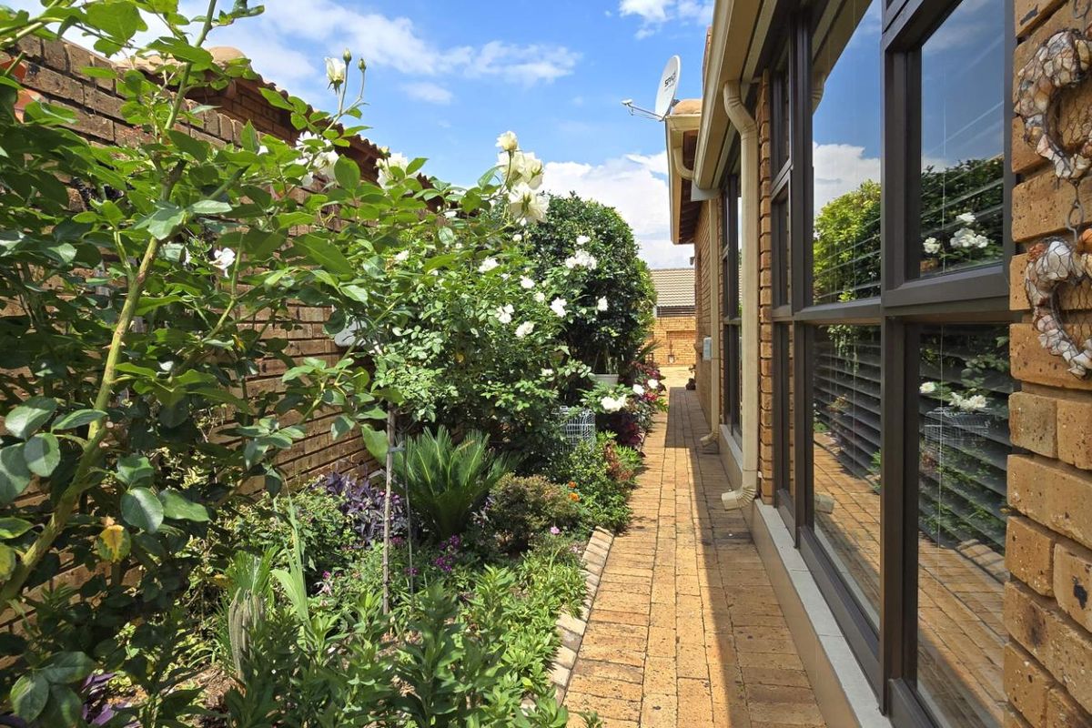 A well-maintained side garden path featuring brick paving, established rose bushes, and a brick boundary wall alongside the property exterior.