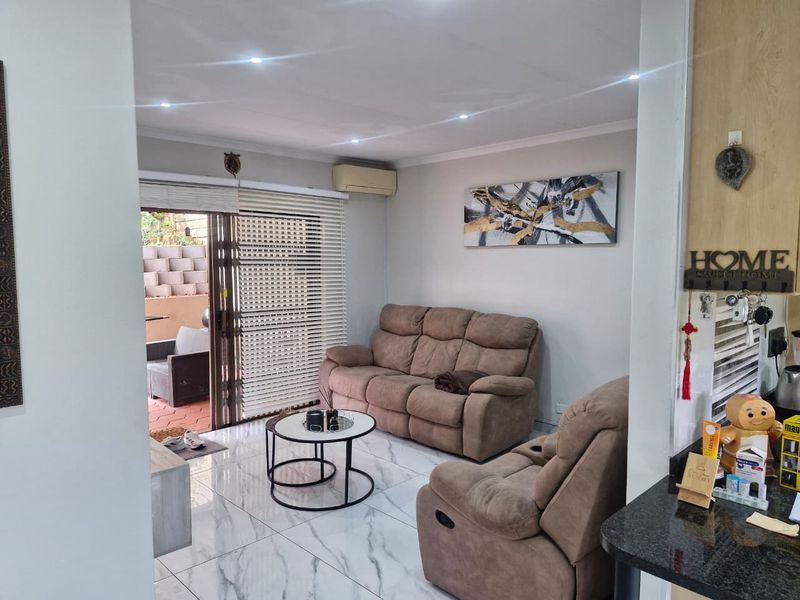 A bright living room featuring marble-look floor tiles, recessed downlighting, and a sliding glass door providing direct access to the outdoor patio area.