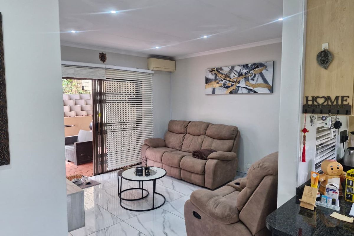 A bright living room featuring marble-look floor tiles, recessed downlighting, and a sliding glass door providing direct access to the outdoor patio area.