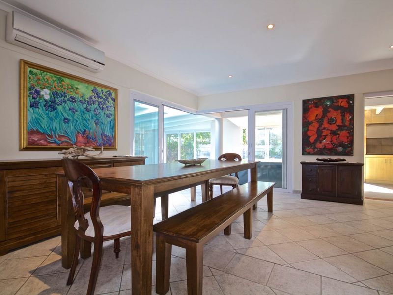 A bright dining room featuring tiled flooring, recessed downlighting, and a wall-mounted split-system air conditioner, with direct access to an outdoor patio area.