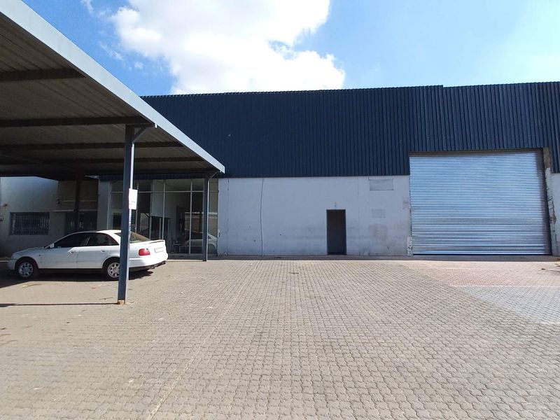 Industrial property exterior featuring a large roller shutter door, covered parking area, and paved forecourt with prominent signage.