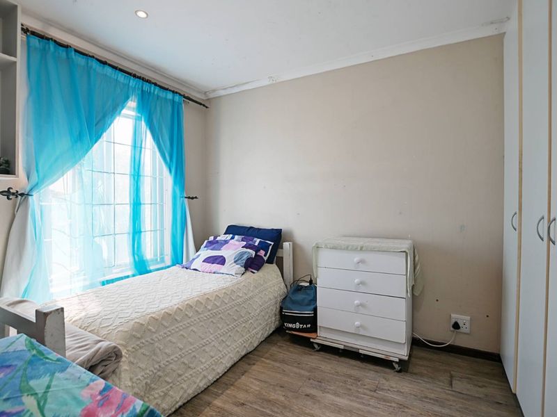 A bedroom featuring laminate flooring, built-in wardrobes, and a window with natural light. The room requires minor cosmetic updates to the walls and ceiling.