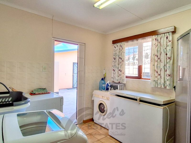 Functional laundry room featuring tiled splashbacks, ceramic flooring, and direct access to the exterior via a folding door.