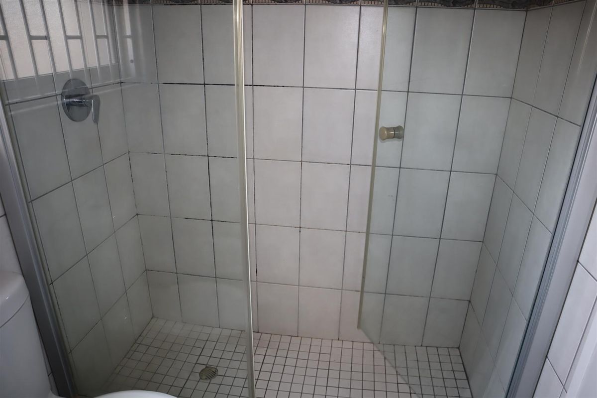 A shower enclosure featuring white wall tiles and a tiled floor, requiring maintenance to address discolored grout and surface grime.